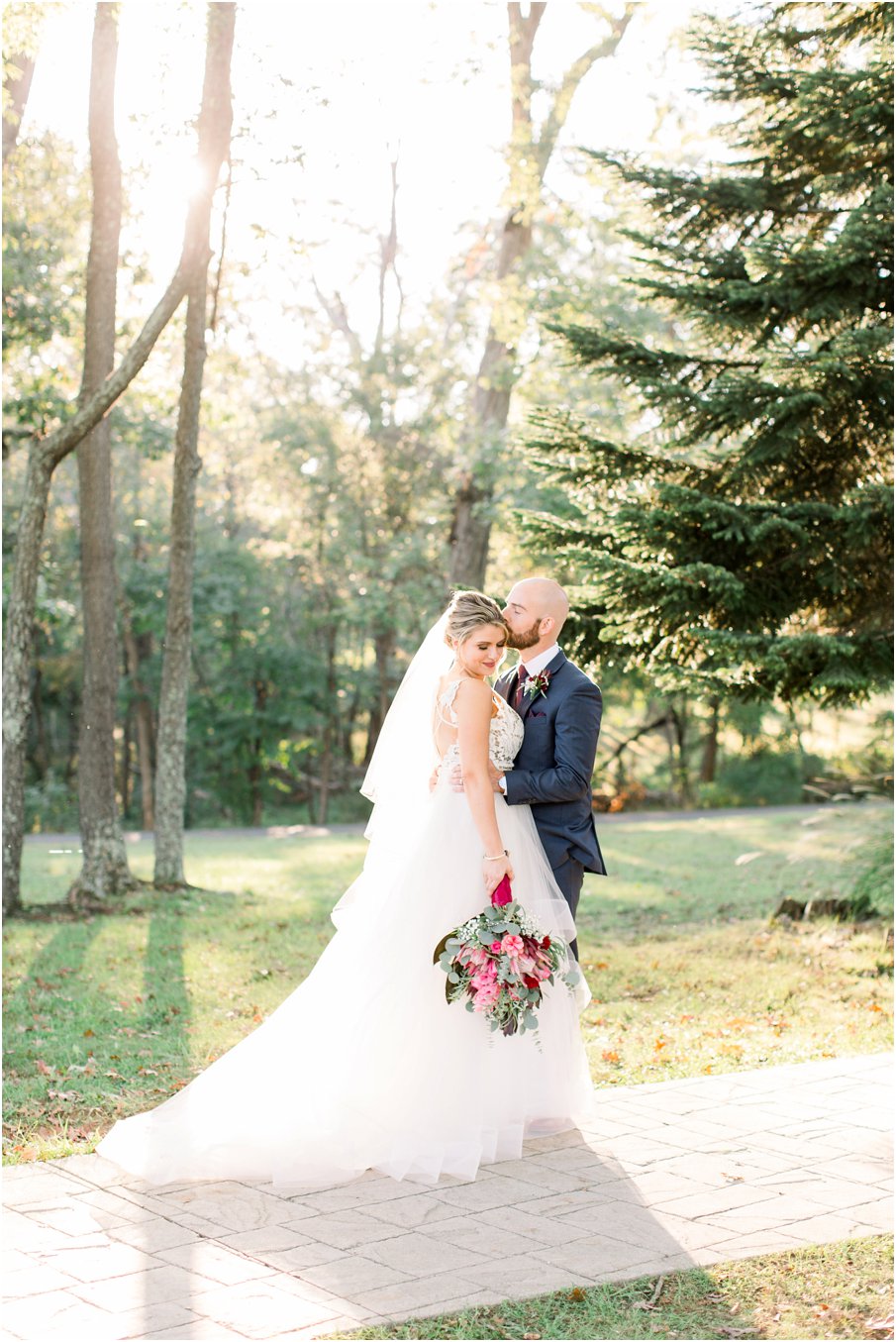 Bride and Groom during sunset at their Rust Manor House wedding. Navy suit, Hayley Paige wedding dress, and burgundy floral accents