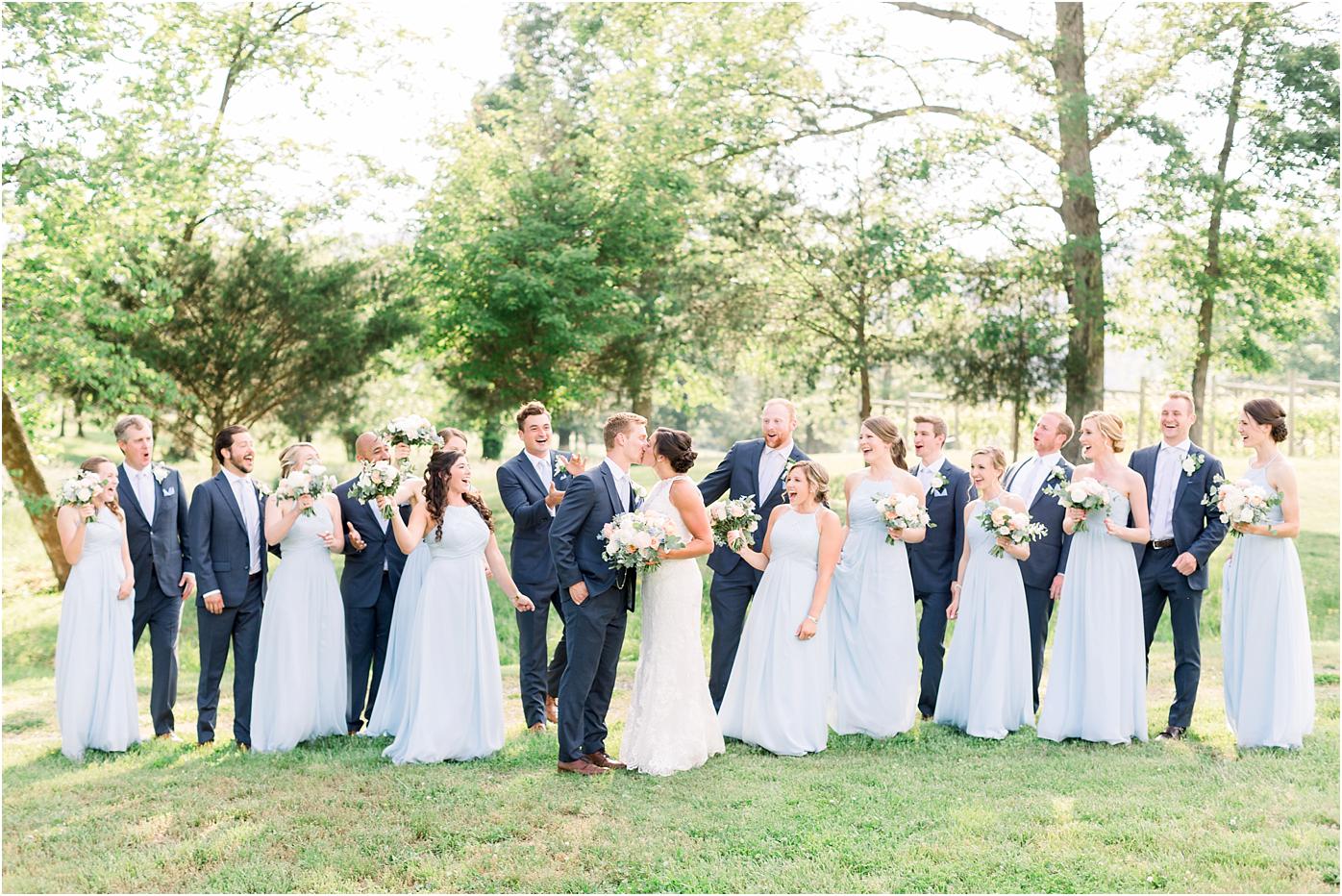 Bridal party cheering the bride and groom on their new marriage. Sky blue bridesmaid dresses, navy suits, and blush and peach bouquets with Veritas winery in the background