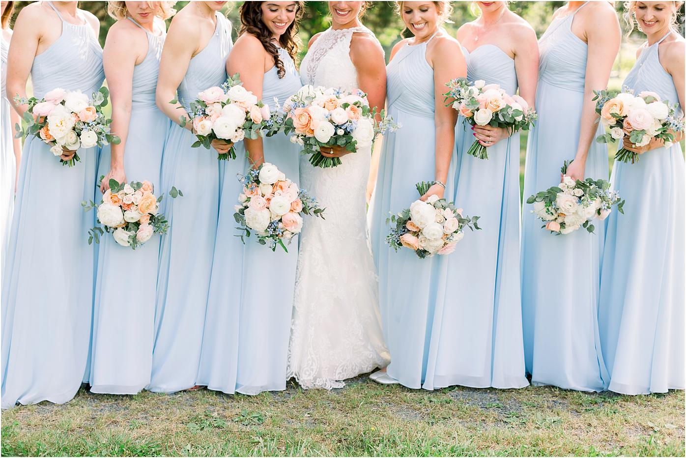 bridesmaids in sky blue dresses holding peach, blush, ivory florals with greenery bouquets