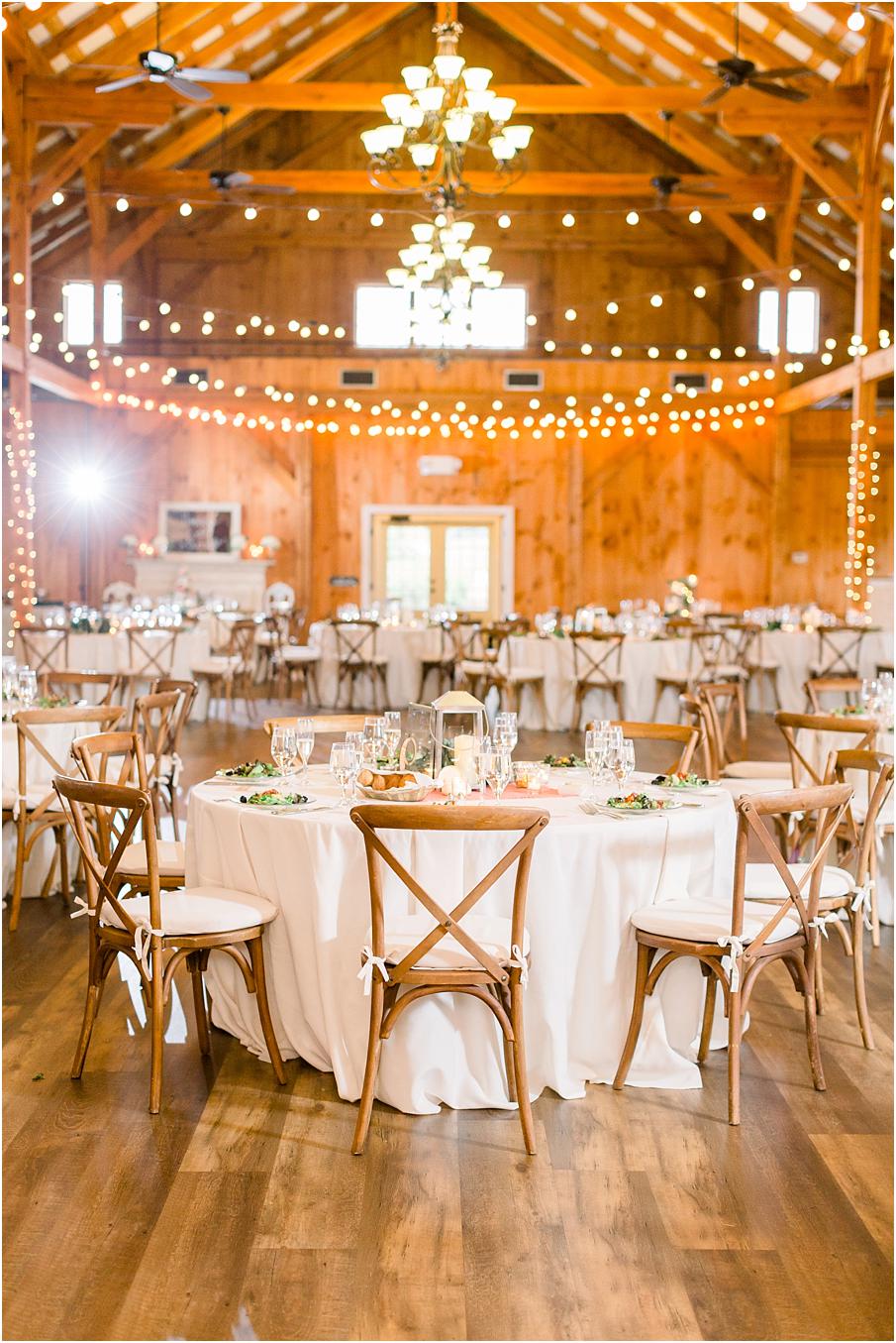 Shadow creek's barn reception layout with white linens, wood cross back chairs, and lantern center pieces