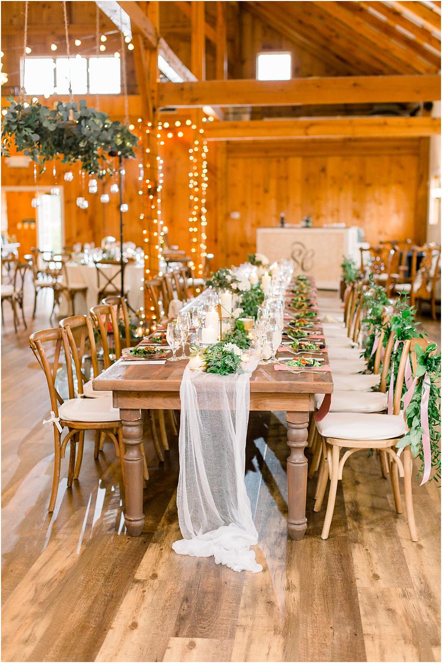 Head table in the barn at Shadow Creek with greenery, lanterns, and white sheer cloth